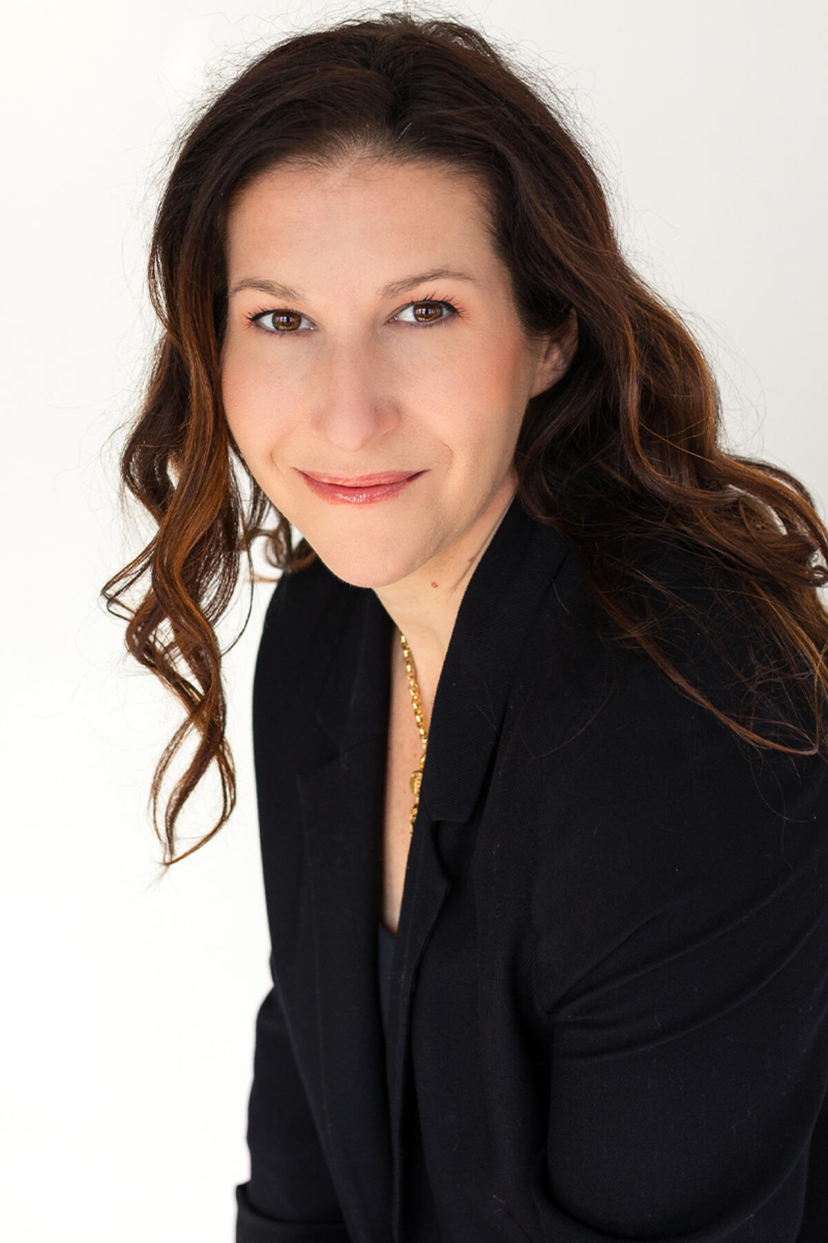 Britt Frank color portrait. Britt is a white person with long brown, wavy hair that ends past her shoulders. She is smiling and is wearing a black suit.