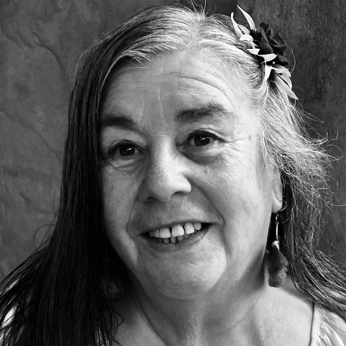 Catalina (Cata) Gomes black and white portrait. Cata is an Indigenous Ramaytush Ohlone woman who has her hair pinned back with a flower as she smiles for the photo.