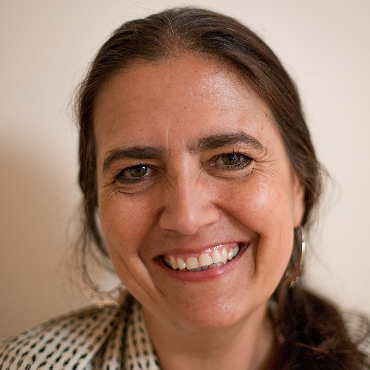 Mireya Alejo Marcet color portrait. Mireya is a Mexican woman who is smiling in this photo and has her brown medium-length hair pulled back into a low pony that is seen on one shoulder. She is wearing a white and black patterned shawl.