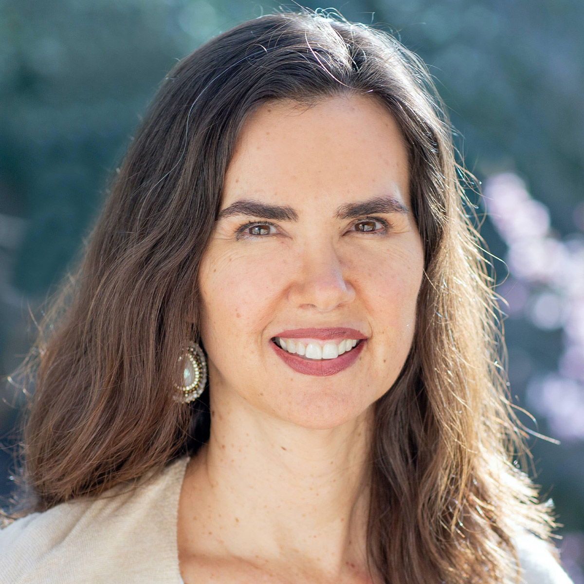 Kristin Neff color portrait. Kristin is a white woman with long, brown hair that goes past her shoulders. She is wearing what appears to be beaded earrings and a light-colored top and is smiling.