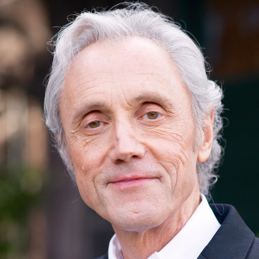 Richard Tarnas color portrait. Richard is an older, white man with short white/silver hair. He is smiling in this portrait and posed in front of a blurred background.