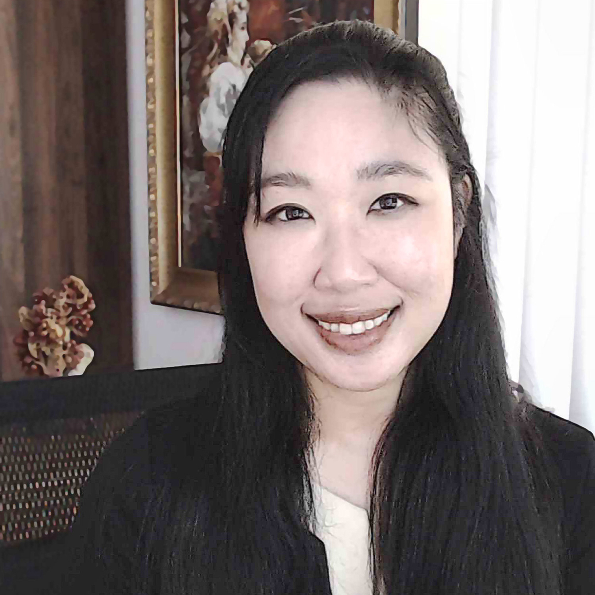 Benebell Wen color portrait. Benebell is Taiwanese American and has long dark hair that goes well past her shoulders. She is smiling in this photo and posed in a room in front of a painting and dried flowers.