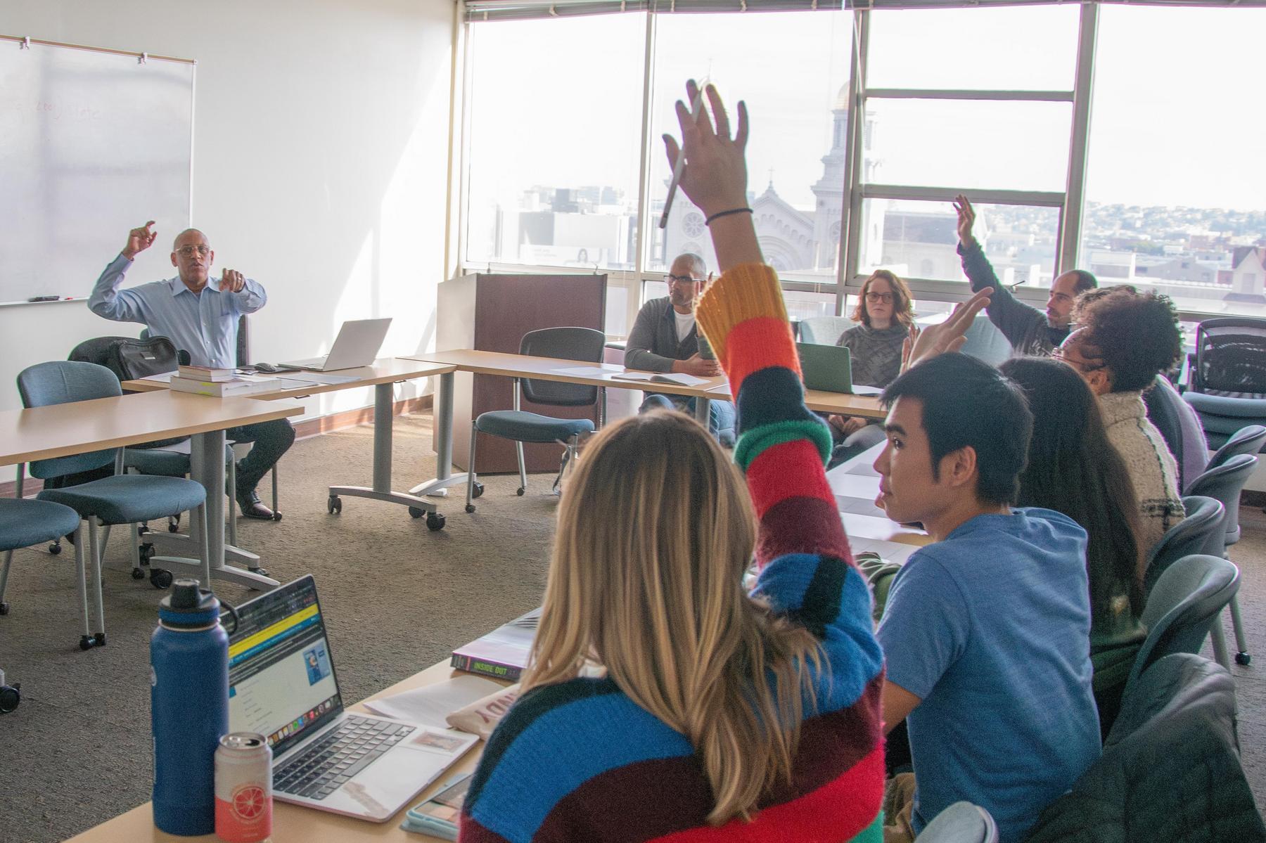 Photo of a teacher pointing at students who have their hands raised
