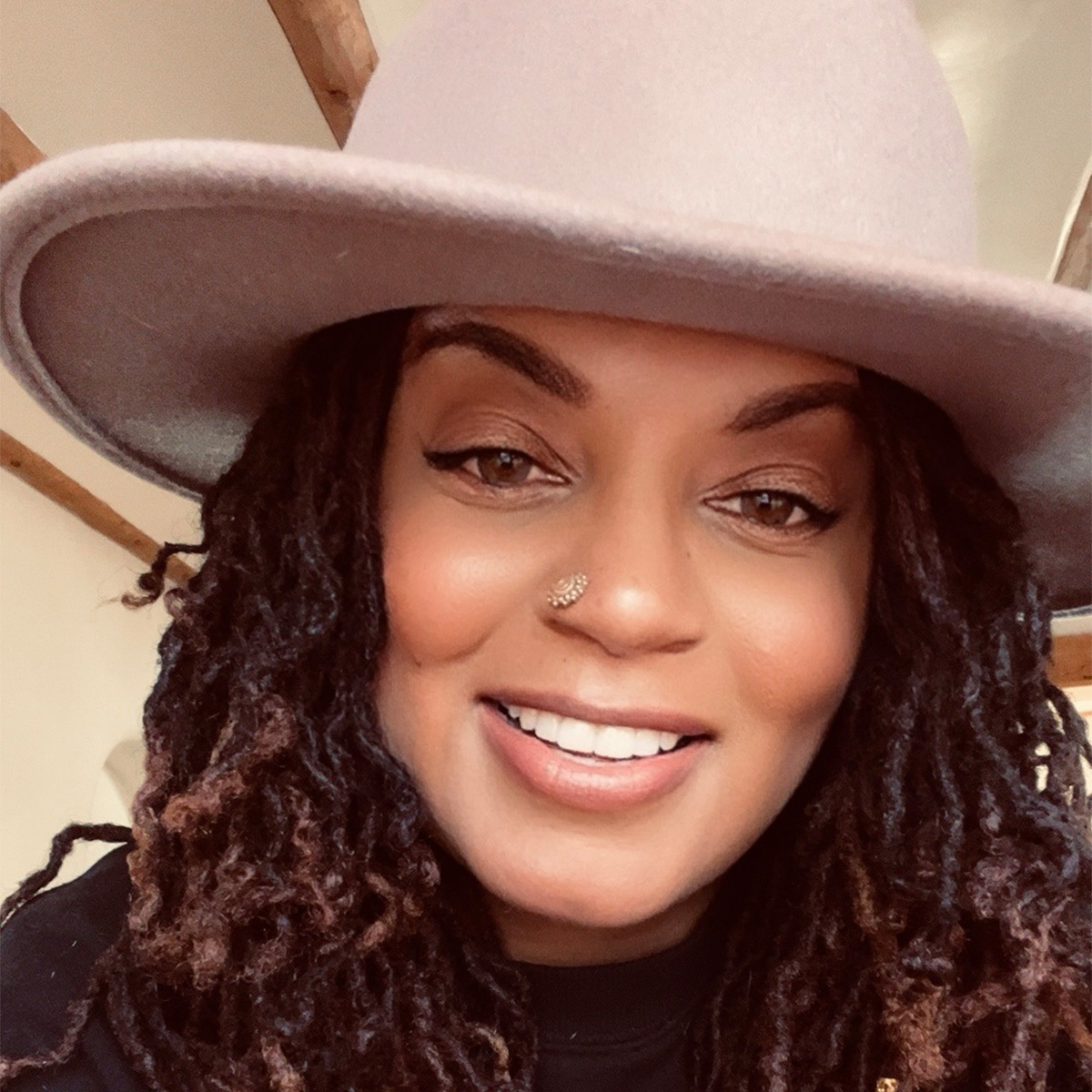 Camara Meri Rajaberi is Great Great Great+ Granddaughter of enslaved Africans and African Freedmen of the Muskogee (Creek) Nation. She is wearing a large brim, tan-colored hat, has dark-brown, medium length twisted/curled hair and is smiling.