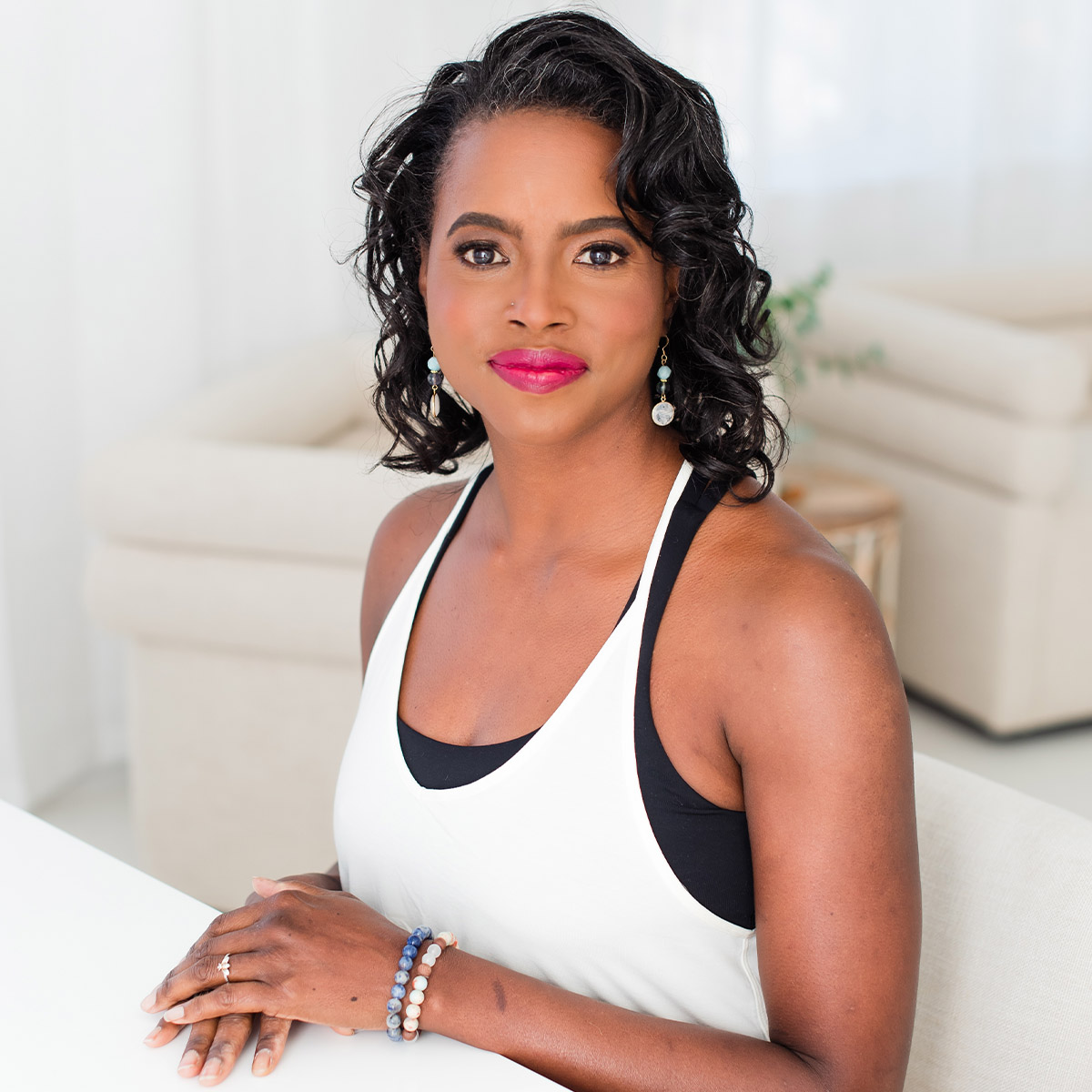 Michelle Cassandra Johnson color portrait. Michelle is a Black woman, with curly, dark brown hair that ends before her shoulders. She is seated and has her hands resting on each other as she looks towards the camera.