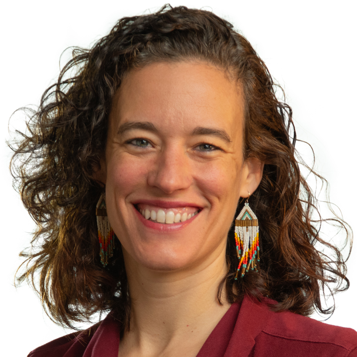 Elizabeth Markle color portrait. Elizabeth is a white woman with medium-length curly hair and is smiling, wearing beaded earrings, a red top, and posed against a white background.