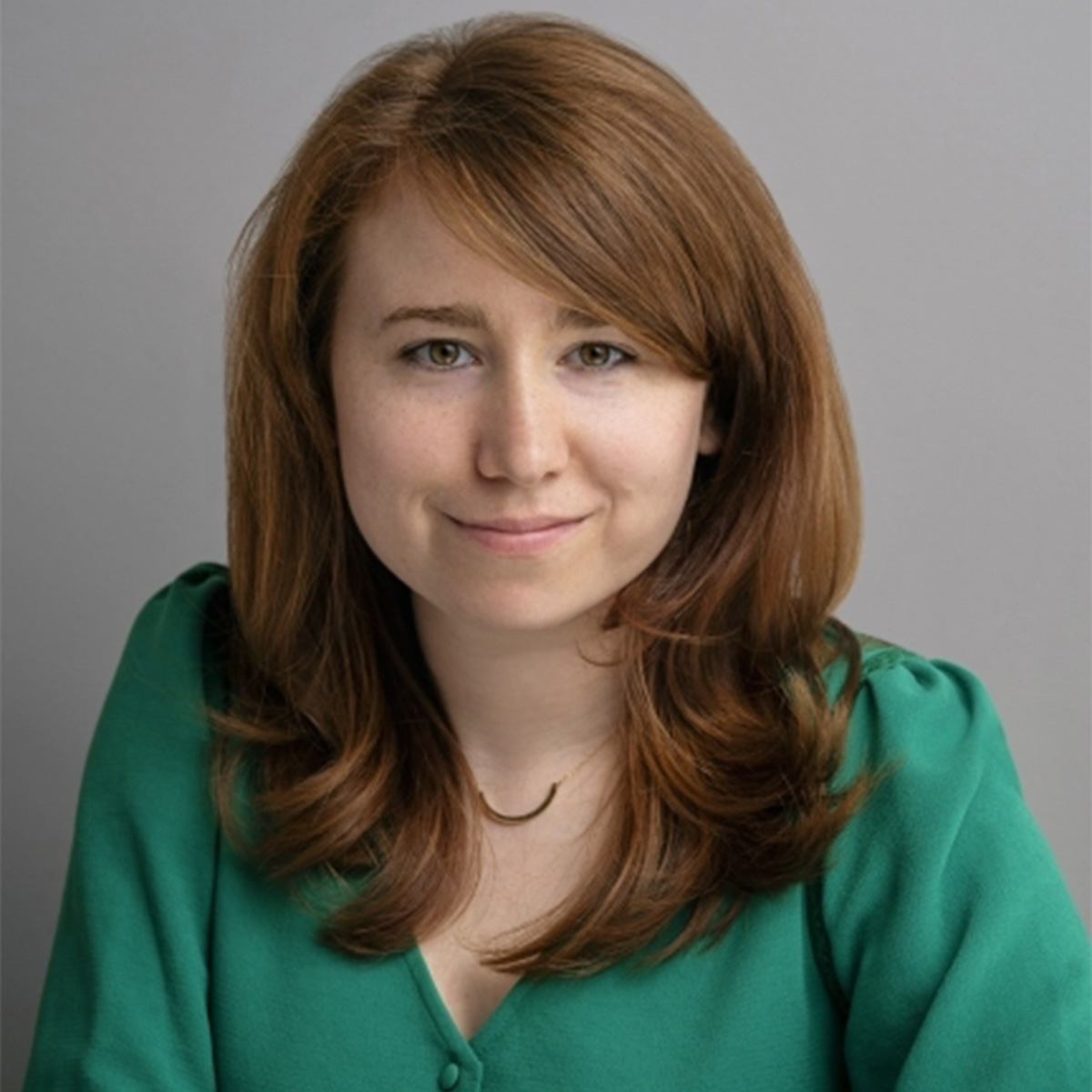 Rhaina Cohen color portrait. Rhaina is a white person with slightly wavy brown hair and is wearing a emerald green top and smiling.