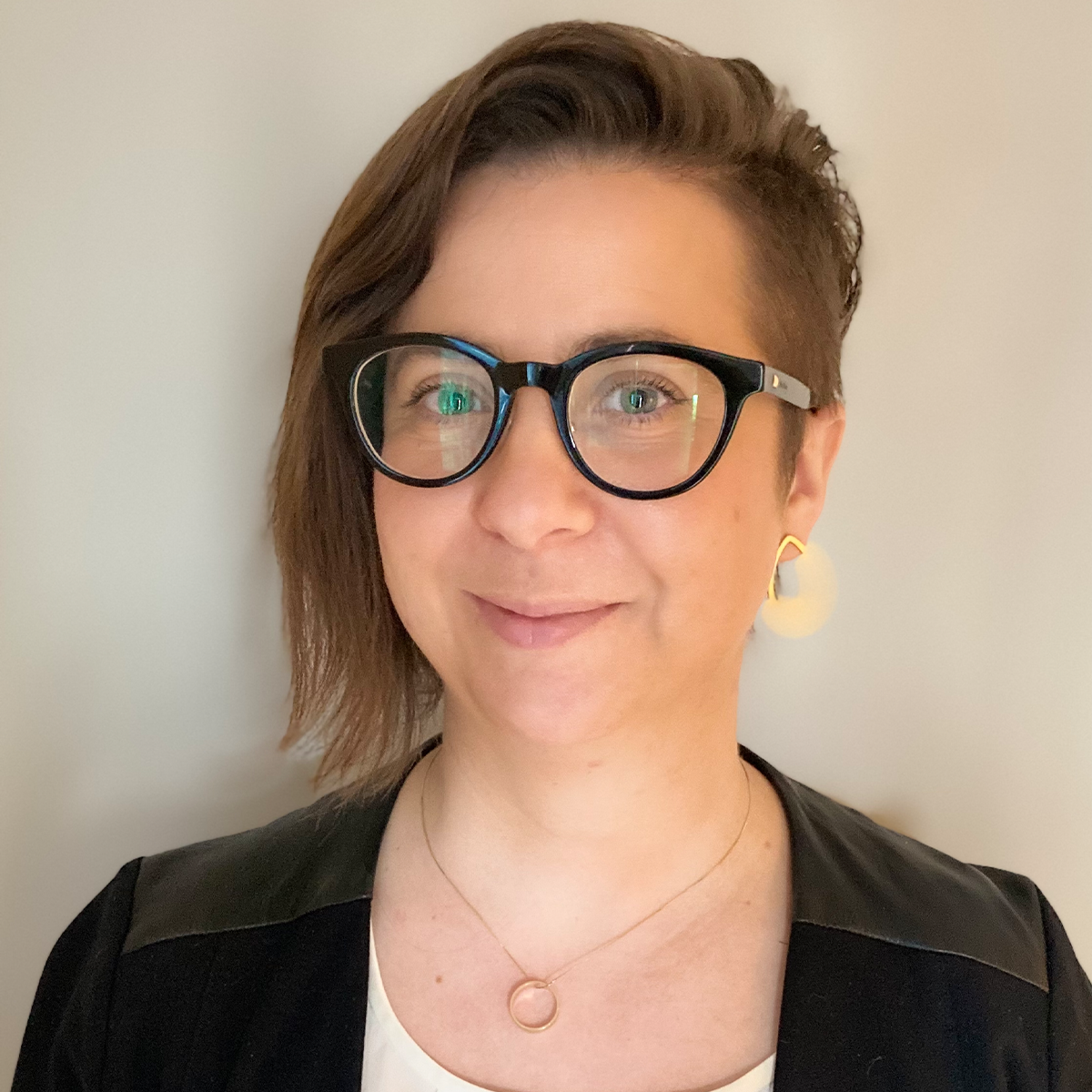 Dr. Anna Corwin color portrait. Dr. Corwin is a white woman with chin-length straight hair that is shorter on one side. She is smiling, wears dark-rimmed glasses, a pendant necklace, and dark-colored top.