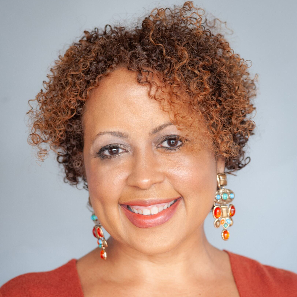 Stacie Yeldell color portrait. Stacie is a light brown skinned person with short curly hair in shades of light and dark brown. She is smiling and is wearing beaded earrings, a dark range top.