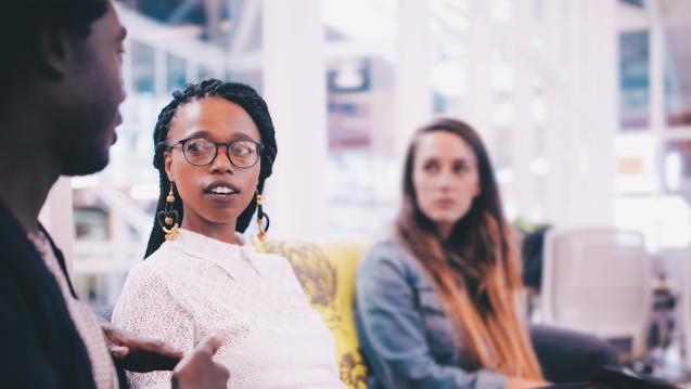 Group of three young professionals sit together on a couch the two on the right are looking at the one on the left. Learn about how to finish your Bachelor degree at CIIS.