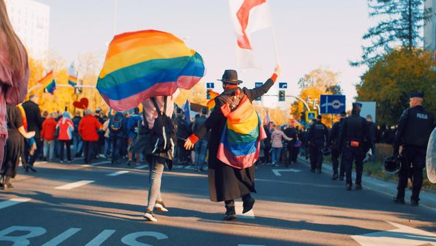 Two people walking in a pride parade holding flags