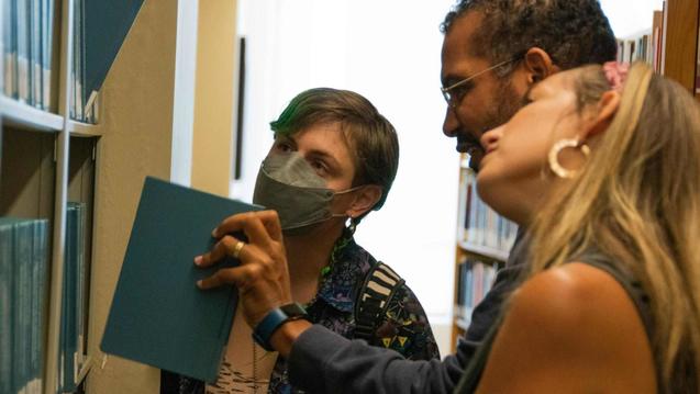 Photo of three people looking at a library bookshelf