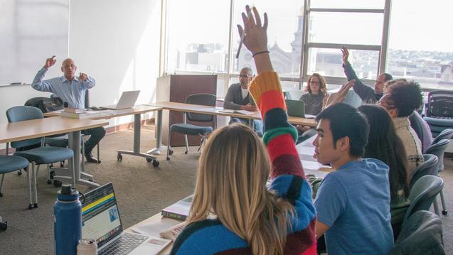 Photo of a teacher pointing at students who have their hands raised