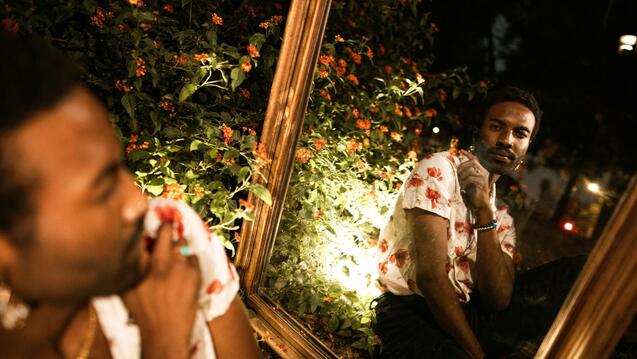Black man with flowers looking at a mirror