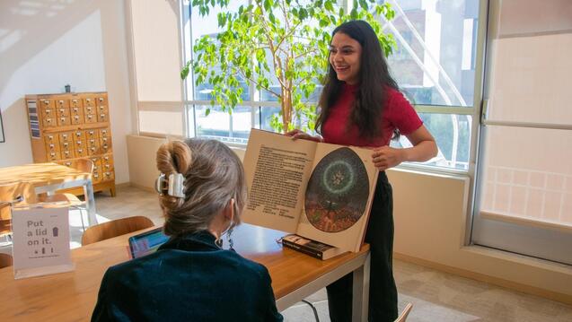 Image of two women in the library, one is holding a book open.