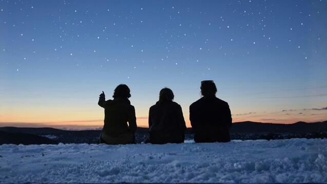 Outline of three people sitting and looking at a starry sky