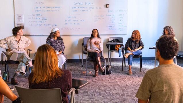 Group of CIIS students sitting chairs in a circle with whiteboard behind them.