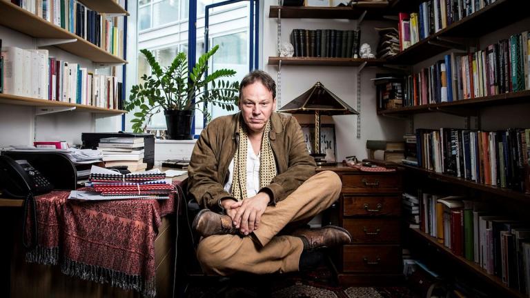 David Graeber sitting in a library cross-legged