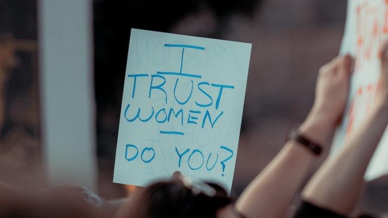 People protesting holding a sign saying "I trust women, do you?"