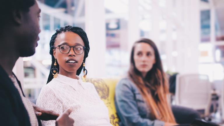 Group of three young professionals sit together on a couch the two on the right are looking at the one on the left. Learn about how to finish your Bachelor degree at CIIS.