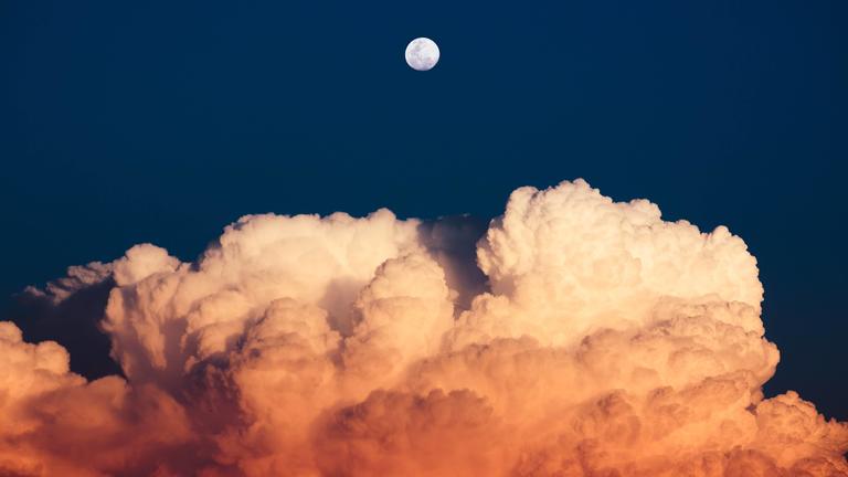 Full moon over clouds in the evening clouds