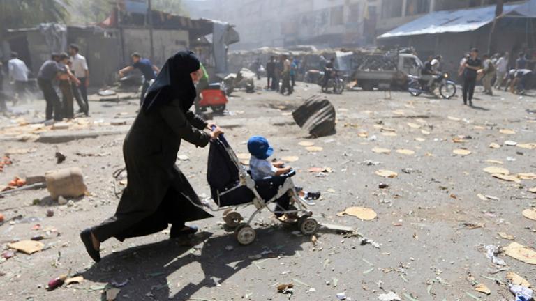 Syrian woman pushing stroller through debris.