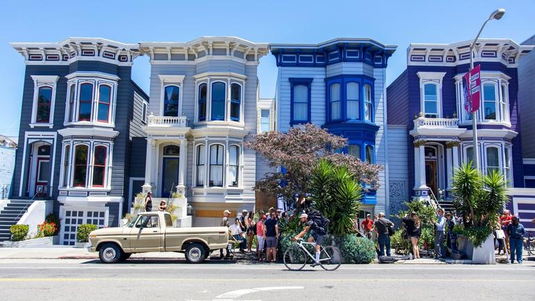 Photo of 4 painted lady style houses in San Francisco with people on the sidewalk