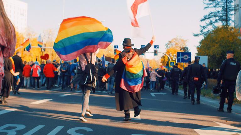 Two people walking in a pride parade holding flags