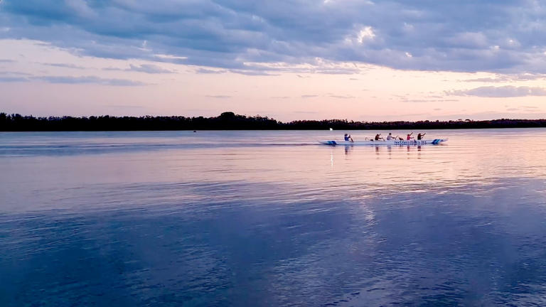 Photo of people rowing on a lake with deep blue hues and cloud reflections