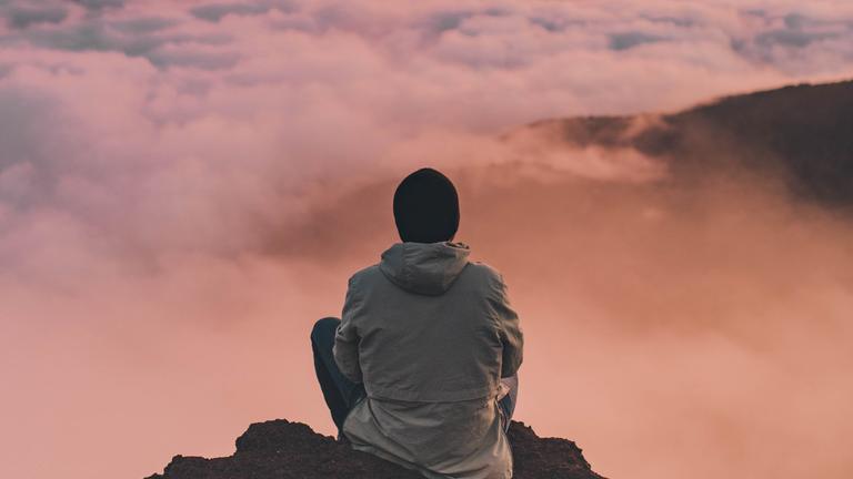 Person sitting on a mountain looking into the sky