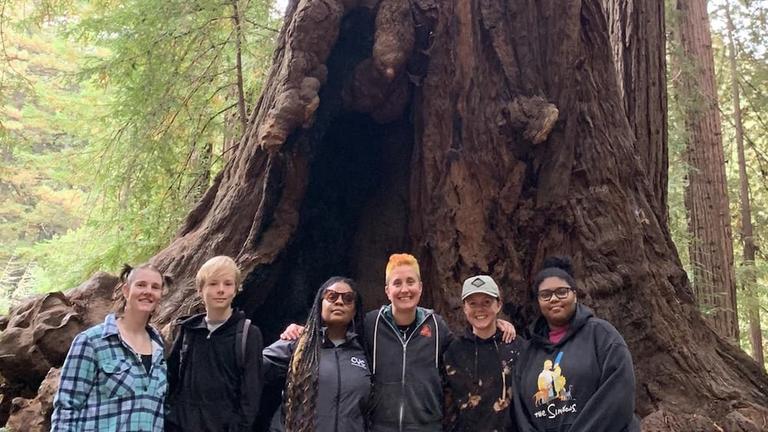 Five program participants and leader Max posing in front of a large redwood tree