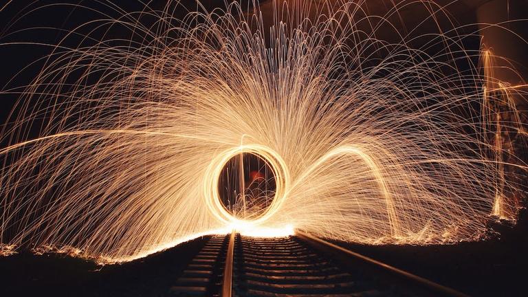 A fire spiral sparkling ahead in looking down a dark distant road or bridge.