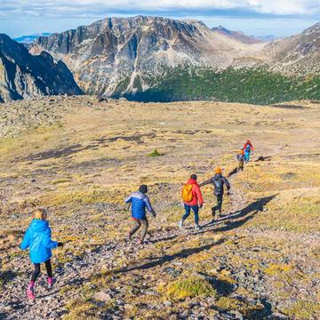 Photo of five people hiking across a sunny meadow surrounded by mountains by Greg Rosenke on Unsplash