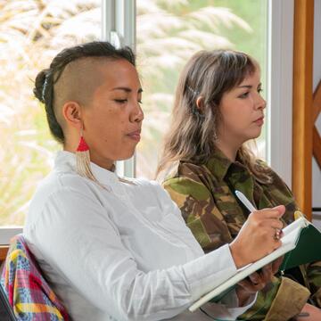 Photo of a person writing in a notebook and taking notes. Woman with partly shaved head and red earrings.