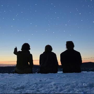 Outline of three people sitting and looking at a starry sky