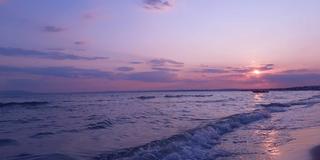Photo of a waves crashing on a beach with a pink and purple sky
