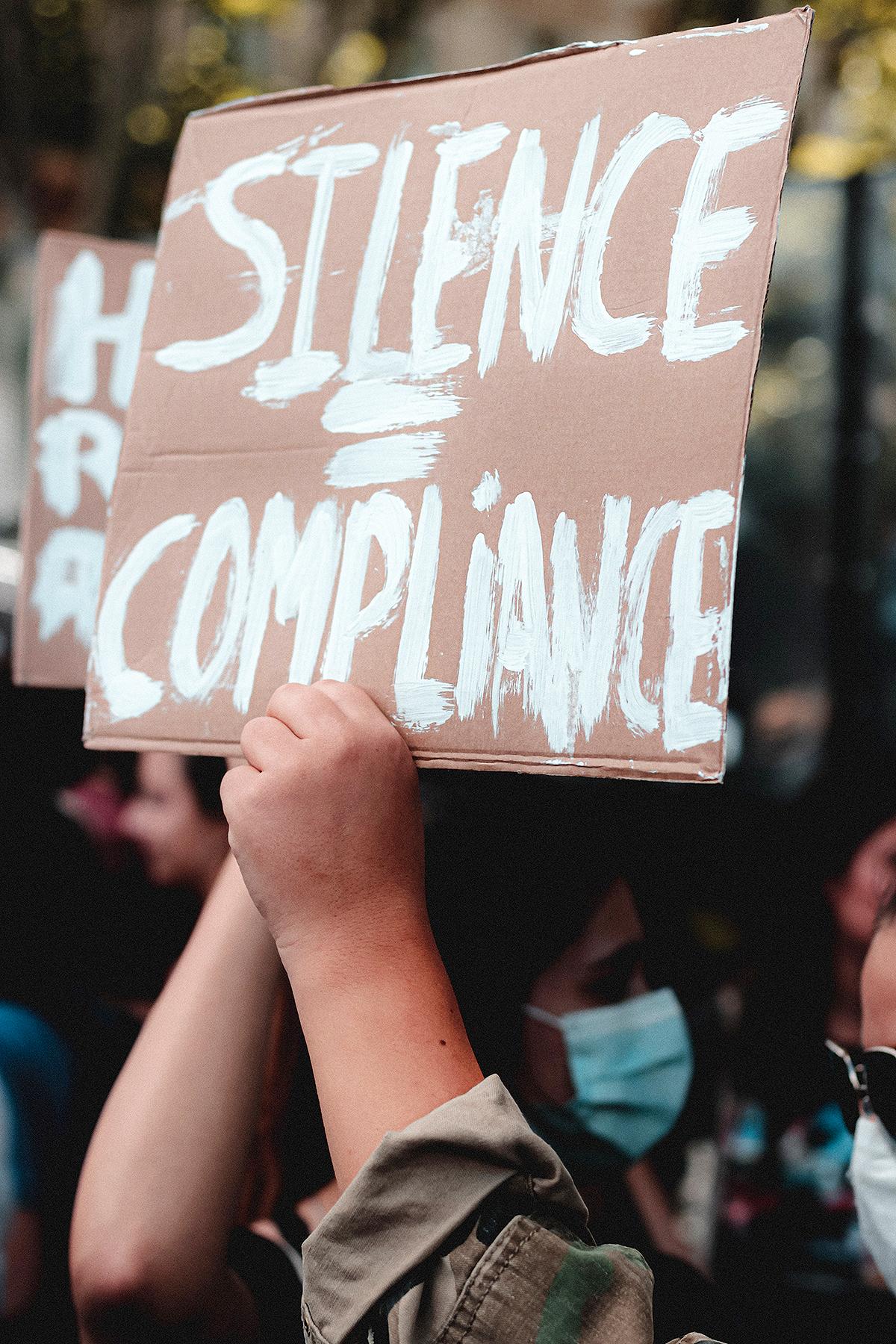 Protest sign reading silence equals compliance