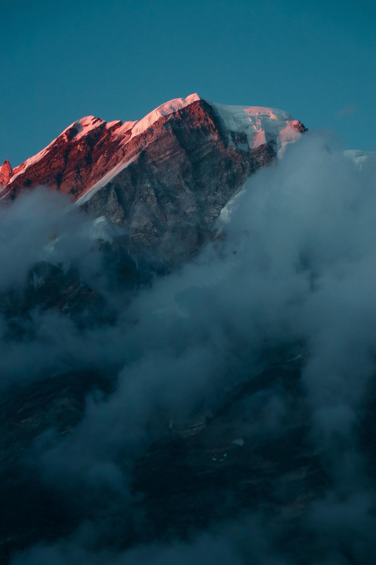 Himalayan mountain appearing with a red tone with blue sky in the background and white clouds in the foreground