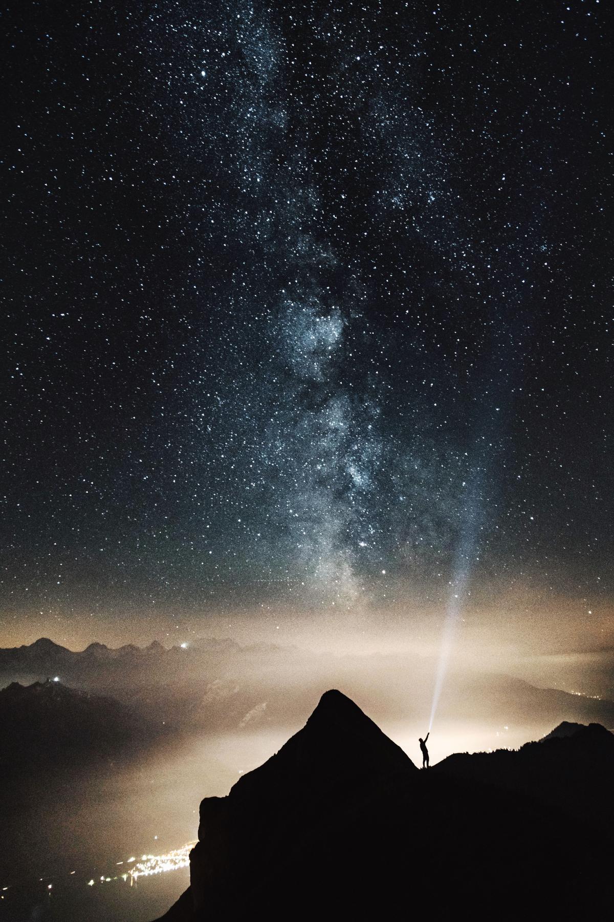 Person standing on a mountain shining a laser into the night sky
