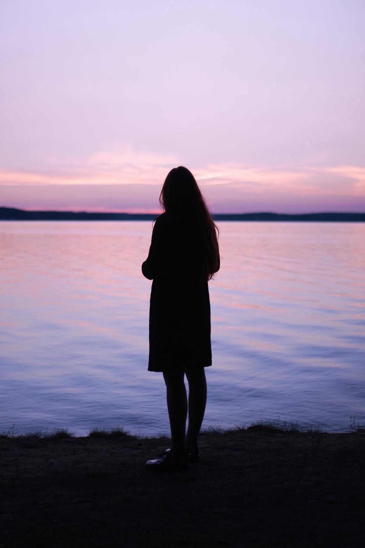 Silhouette of a person standing in front of a still purple lake