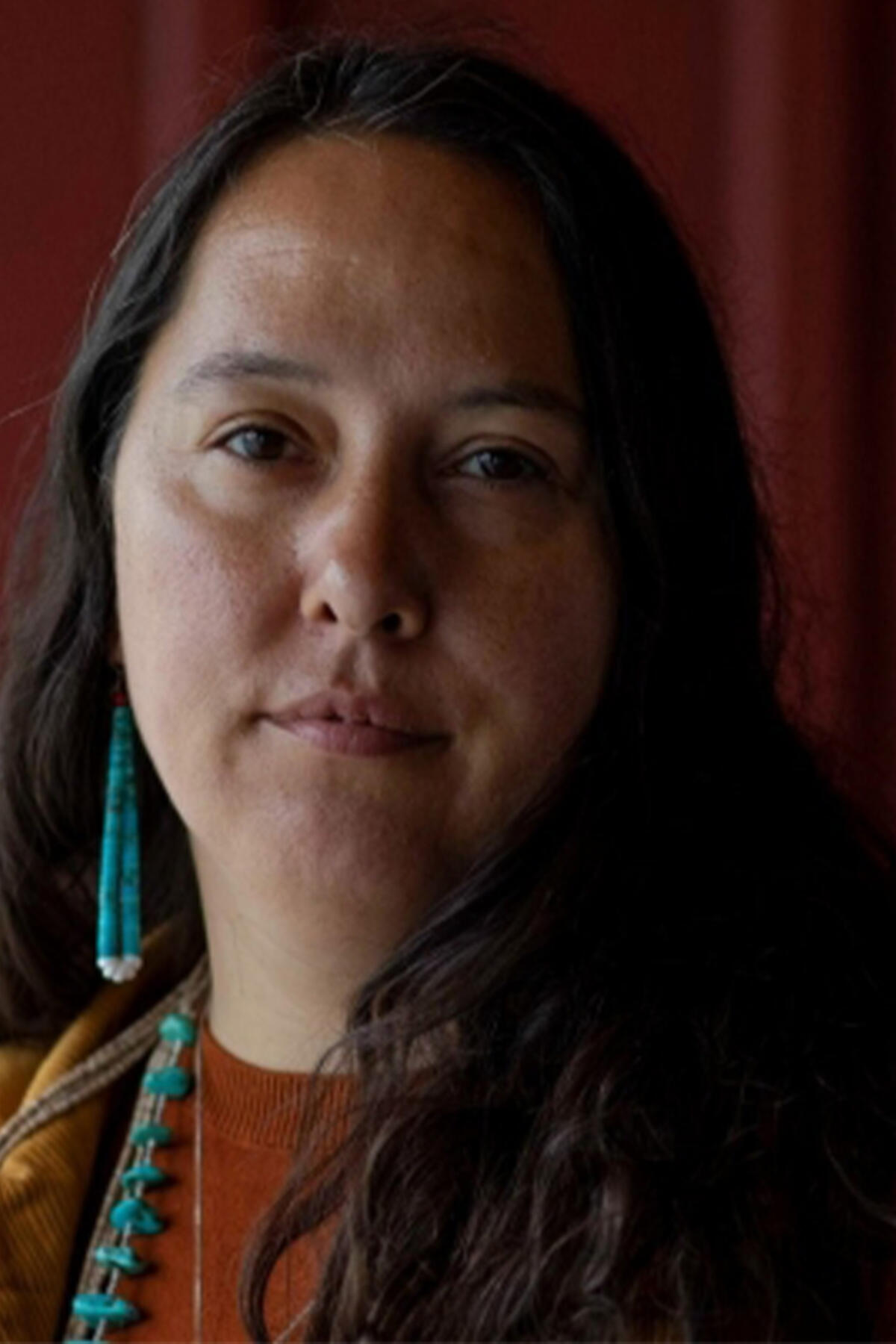 Rowen White color portrait. Rowen is from the Mohawk community of Akwesasne and is standing in a field of plants, and crops holding a woven basket in front of her and smiling.
