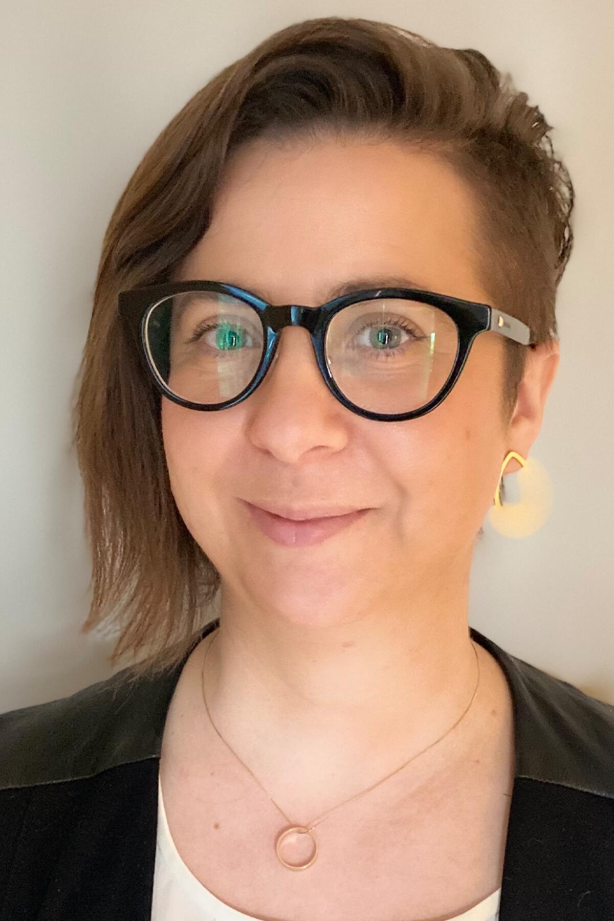 Dr. Anna Corwin color portrait. Dr. Corwin is a white woman with chin-length straight hair that is shorter on one side. She is smiling, wears dark-rimmed glasses, a pendant necklace, and dark-colored top.
