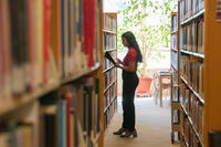 female student reading book in the stacks