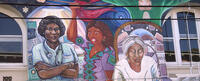 Mural with three women of colour: a medical doctor, a woman holding a red flag and an elder woman.