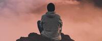 A photo of the back of someone sitting on a boulder with a pink cloudy sky