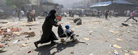 Syrian woman pushing stroller through debris. 