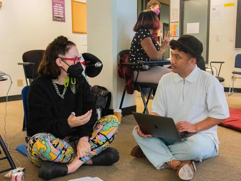 Photo of two students sitting on the floor of a classroom in discussion