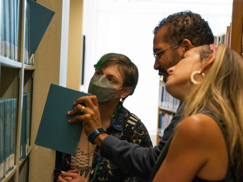 Photo of three people looking at a library bookshelf