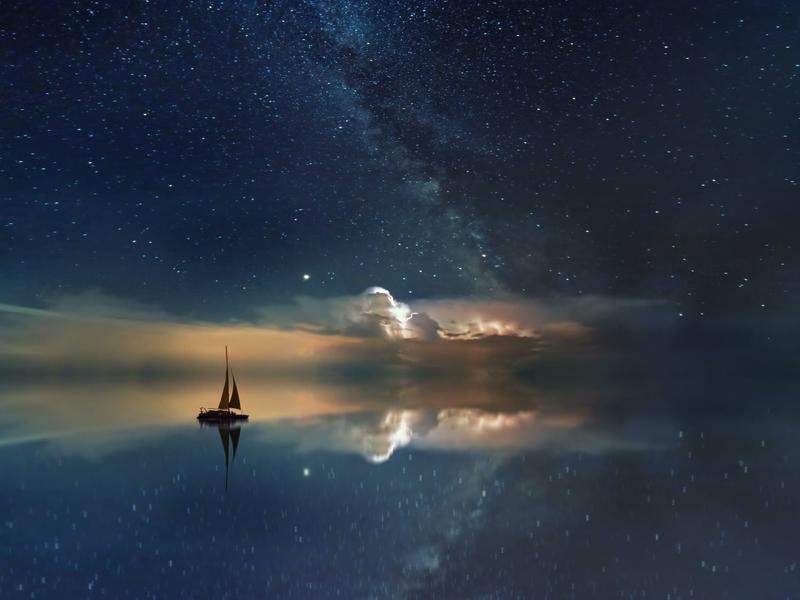 Image of a sailboat on a vast water reflecting the stars