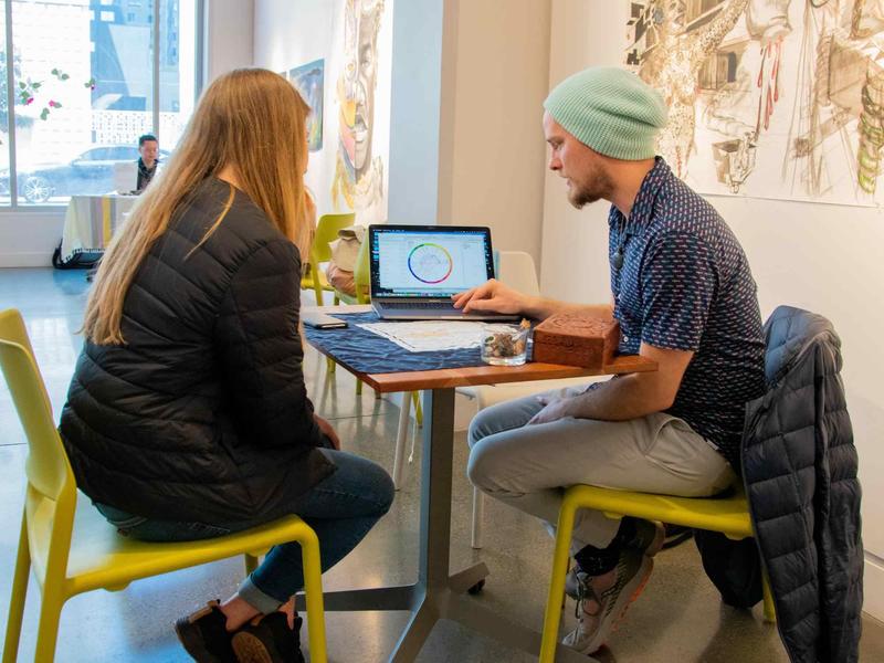 Photo of two people seated at a cafe table looking at a laptop